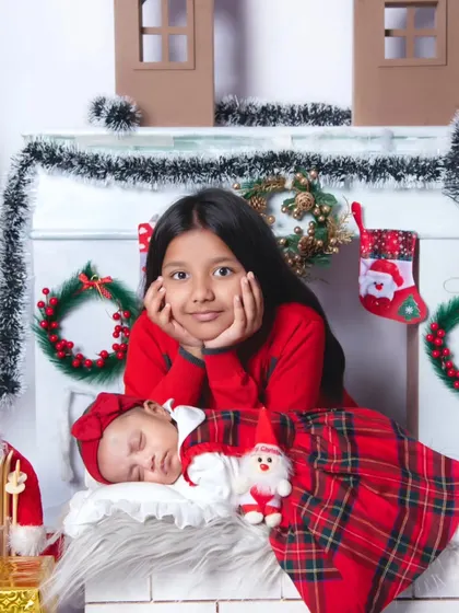 An older sister proudly watches over her sleeping newborn sibling. This heartwarming moment was captured during our special Christmas-themed mini-sessions.