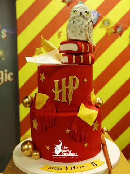 A truly magical birthday cake for the Harry Potter theme. This two-tiered red cake is decorated with the HP logo, a Gryffindor scarf, golden snitches, and topped with a detailed Hedwig the owl figure.