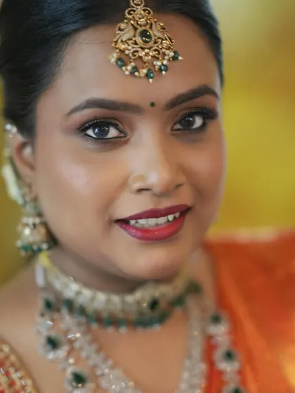 A close-up of a classic engagement makeup look. The focus is on beautifully defined eyes and a rich red lip, paired with traditional maang tikka and layered necklaces.