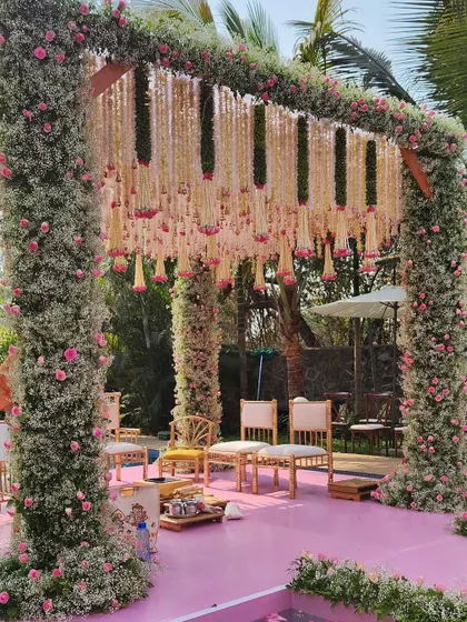 A poolside mandap in Alibaug, with pillars covered in baby's breath and pink roses, and a delicate floral ceiling. The pink aisle is set over the pool for a unique touch.