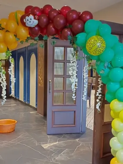 A vibrant balloon archway at the entrance of a jungle-themed party. The arch uses green, yellow, and red balloons with decorative vines to create a welcoming jungle gate for guests.