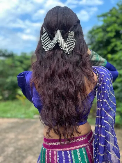 The hairstyle is just as important for a festive look. Here, soft waves are accented with a statement silver hair accessory that complements the traditional Navratri outfit.