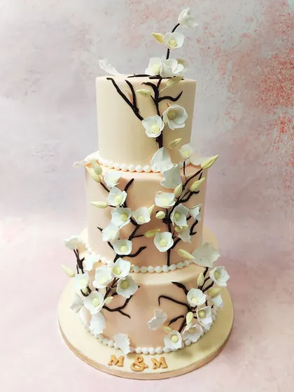 We create a breathtaking centerpiece with this three-tiered cherry blossom wedding cake. Delicate, handcrafted sugar cherry blossoms gracefully climb dark branches against a soft blush-colored fondant, embodying the beauty and elegance of a spring wedding.