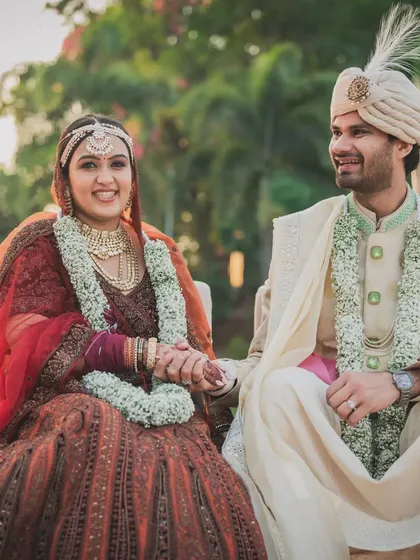 A candid shot of the couple holding hands, seated at their wedding ceremony. The decor is designed to create a beautiful frame for these intimate moments.