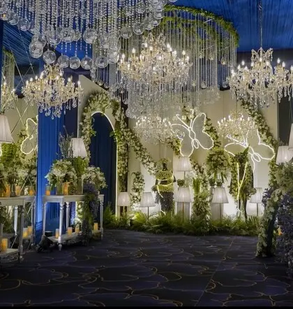 The entrance to the main hall, where guests are greeted by a forest of flowers, illuminated butterfly installations, and a ceiling dripping with crystal chandeliers. It’s a truly magical welcome.