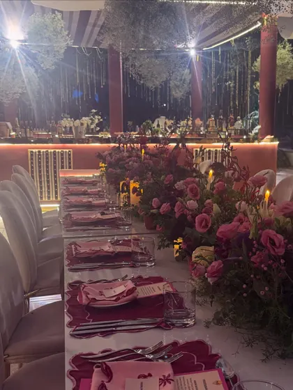 A finale dinner designed to celebrate two families becoming one. The tables are adorned with lush pink and red floral arrangements and candlelight, creating a warm and romantic atmosphere.