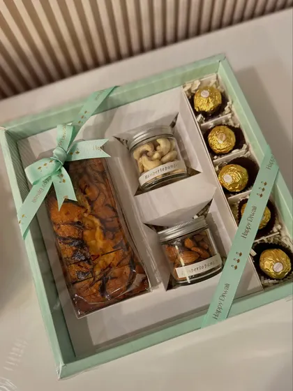 Our "Celebration Box" is a simple yet elegant Diwali gift. It features a delicious marble tea cake, jars of premium almonds and cashews, and Ferrero Rocher, all tied with a "Happy Diwali" ribbon.