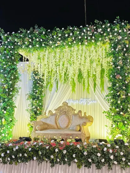 A full view of the greenery arch stage, showing the lush floral border and the elegant gold and white seating.
