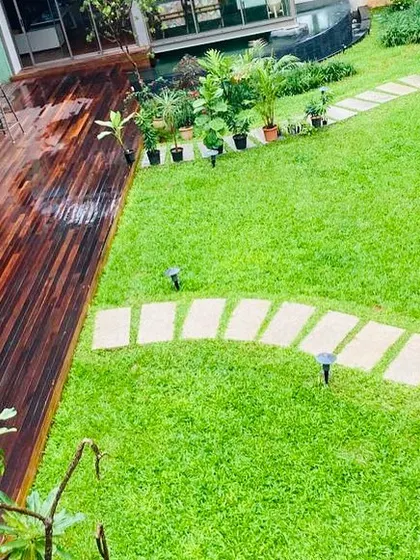 An aerial view of a residential garden showing the relationship between the wooden deck, the expansive lawn, and the stone pathway. Our designs focus on creating a harmonious flow between different outdoor elements.