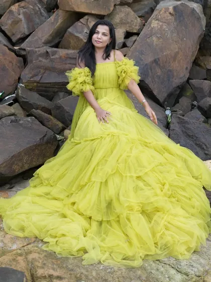 A solo shot of the woman in the yellow ruffled gown, showcasing its volume and dramatic texture against the rocks.