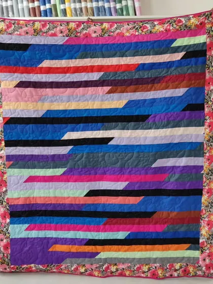 A "jelly roll" race quilt with diagonal stripes of color. This modern design is framed with a beautiful floral border.