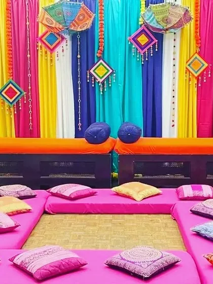 A vibrant floor seating arrangement for a Mehendi or Sangeet event. The decor features multi-colored drapes and dozens of colorful cushions for guest comfort.