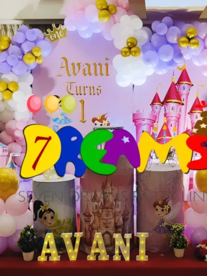 A magical princess castle theme for a first birthday party. This setup includes a large castle backdrop, custom character stands, marquee lights with the birthday girl's name, and a full balloon arch in pastel and gold.