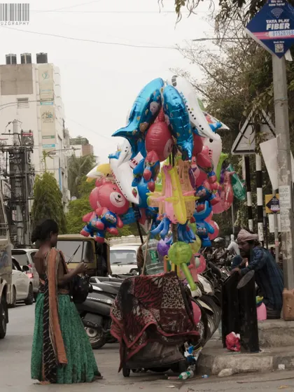 A balloon vendor on a busy street corner, a splash of color in the urban landscape. This image tells a story of small joys and daily hustle.