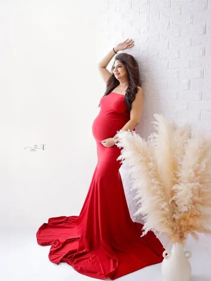 A confident and stylish portrait. The mom-to-be poses in a striking red gown against a clean white brick wall, creating a modern and chic look.