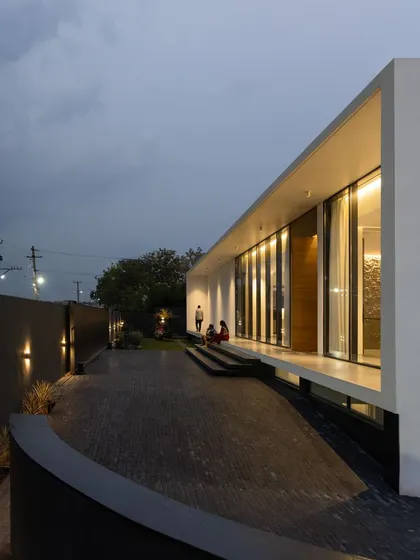 An evening view of the courtyard house. The lighting design highlights the home's clean lines and its connection to the outdoors, as the interior glow spills out onto the wrap-around terrace and landscaped pathway.