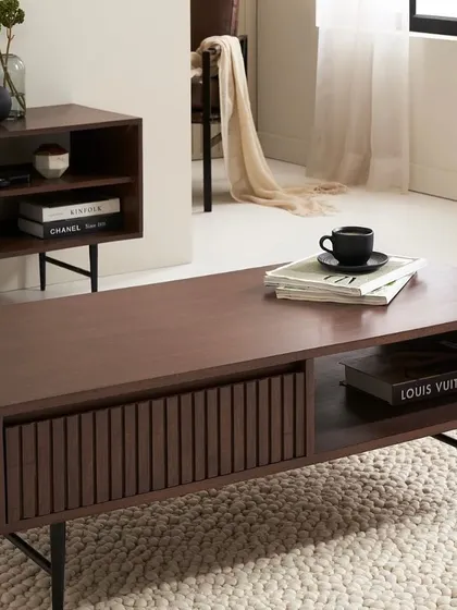 A styled shot of the coffee table from the collection, showing its storage capabilities and sleek design. The focus is on both aesthetics and functionality.