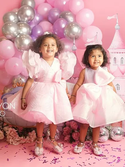 A fairytale dream come true for two sisters. Dressed in beautiful pink gowns, they pose in front of a magical castle backdrop.