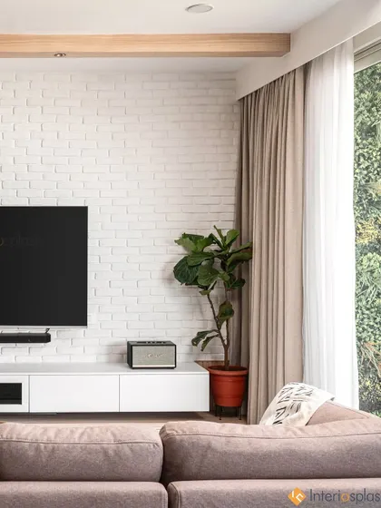 This living room features a clean, white brick accent wall for the TV unit, creating a modern yet rustic texture. The large window allows for plenty of natural light, making the space feel bright and airy.