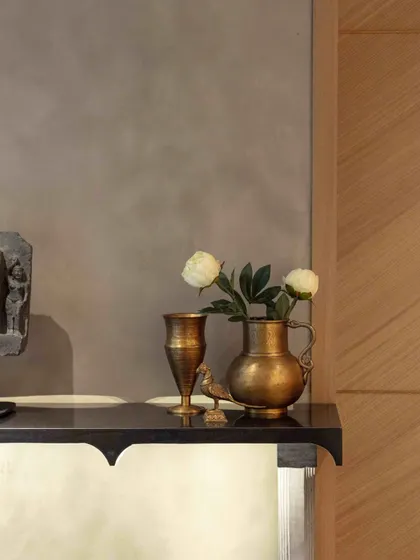 A detail shot showing the textural interplay of materials in the basement lobby. The smooth, cool surface of the console contrasts with the warm brass of antique vessels and the angular grain of the Koto veneer paneling.