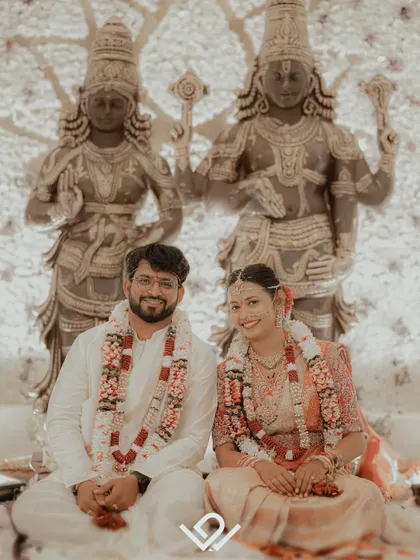A couple seated before deities during their Hindu wedding ceremony, a portrait that blends divine blessings with their personal commitment.