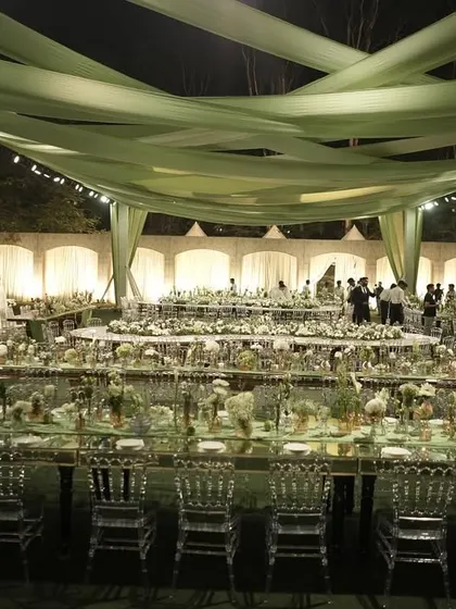 A breathtaking gala dinner setup under a canopy of sage green drapes, with long mirrored tables and clear chairs creating a modern and elegant look.