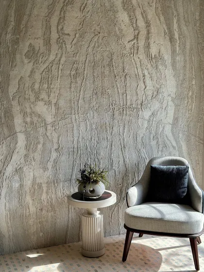 Here, the armchair is set against a dramatic, full-height textured wall. This composition highlights the chair's simple, elegant form, allowing it to stand as a quiet statement piece within a texturally rich environment.