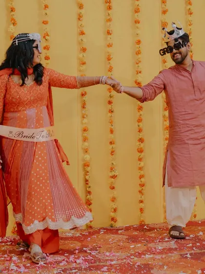 The bride and groom share a dance during their Mehendi or Haldi event. The "Bride to Be" sash and fun props add a playful touch to the celebration.