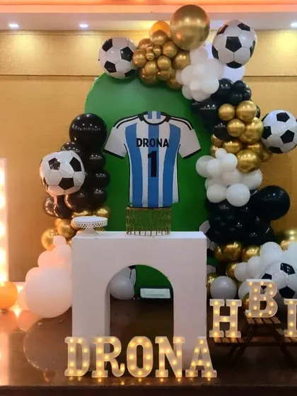 It's a goal! We scored with this football theme for Drona's first birthday. The setup includes a jersey-shaped cake stand, football-themed balloons, and a light-up number "1" against a green and gold backdrop.