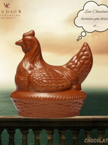 A realistic chocolate hen sitting in a basket, crafted entirely from rich milk chocolate with detailed feathers.