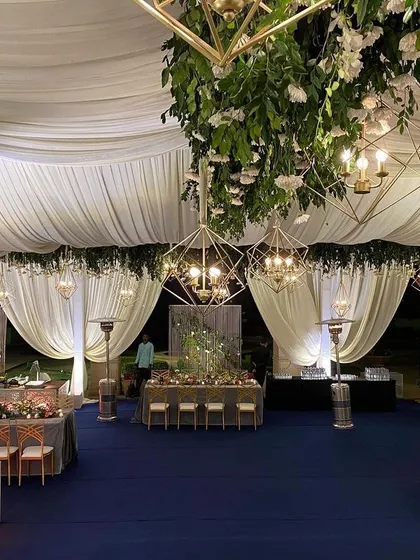 An entrance view of a sophisticated reception hall. The design uses layers of soft white drapes and hanging floral installations to create depth and guide the eye towards the main event space.