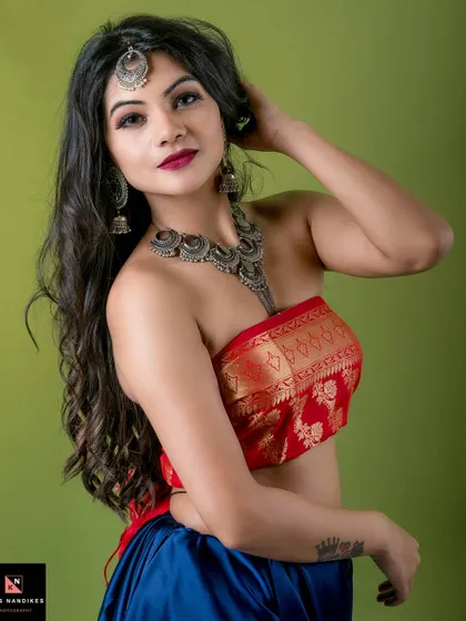 Another angle from the 'Divine' series, this portrait focuses on the model's expressive look and traditional jewelry. The combination of the red top, blue skirt, and silver accessories creates a striking color palette.
