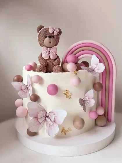A cute and pastel teddy bear cake with butterflies and a rainbow.