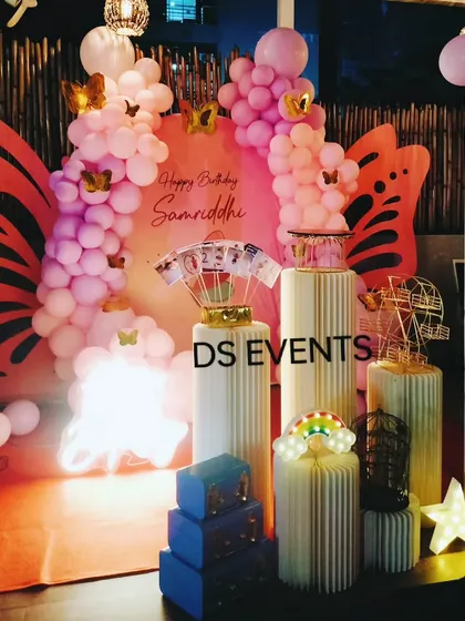 This enchanting butterfly-themed decoration features large, custom-made butterfly wings as a central backdrop element. The pink balloon garland and elegant ribbed plinths complete this beautiful setup for a magical birthday.