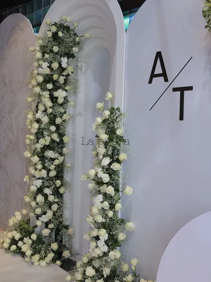 A close-up of the floral decor, showing arches adorned with lush white roses and baby's breath. The couple's initials were added in a clean, modern font, personalizing the elegant design.