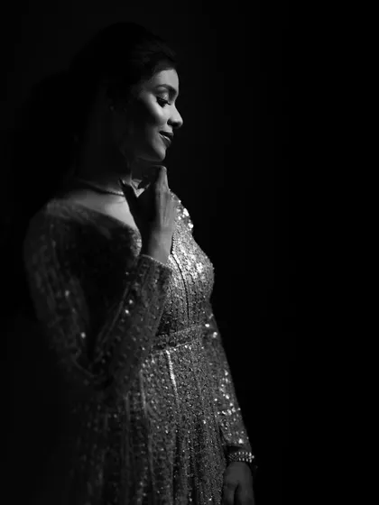 A timeless black and white portrait. The soft light catches the sparkle of her dress, while her gentle smile and pose convey a feeling of quiet happiness and grace.