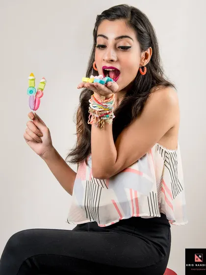 A playful and colorful concept shoot titled 'CANDIES & MARSHMALLOWS'. The model's joyful expression as she interacts with sweets captures a sense of childlike innocence and fun.