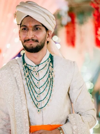A portrait of the groom, looking regal in his white sherwani, multi-layered green necklace, and turban.