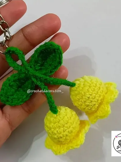 A handmade crochet keyring featuring two yellow lily of the valley flowers and a leaf. It's a beautiful and practical little accessory.