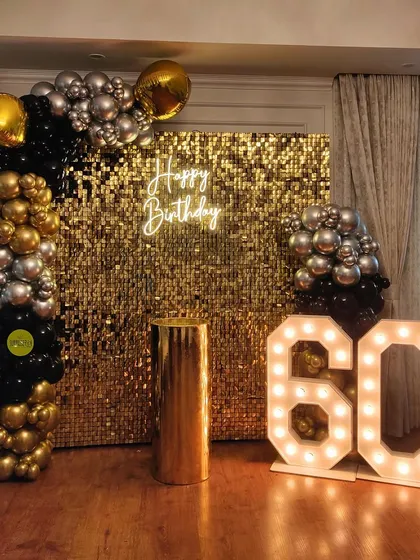 A grand 60th birthday setup with a gold sequin wall, a black and gold organic balloon arch, and oversized marquee numbers. This decor is all about making a bold and luxurious statement.