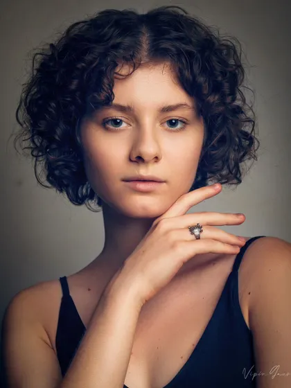 A classic headshot for a model's portfolio. The lighting is designed to accentuate her features and curly hair, while the pose is simple and direct, which is what agencies look for.