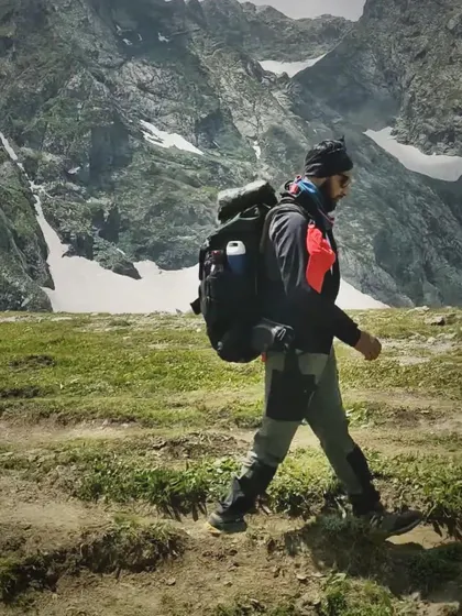 A trek leader with a full pack walks through the alpine terrain of Kashmir, showcasing the endurance and preparation required for these high-altitude expeditions.