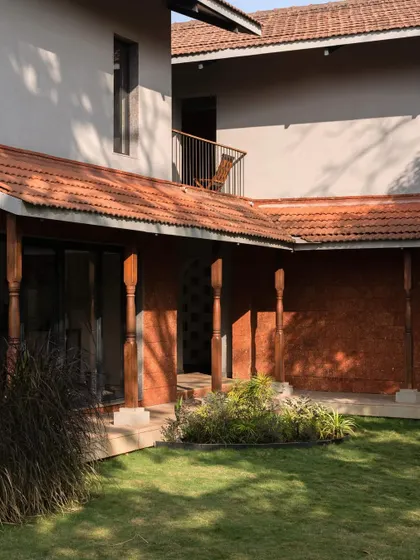 The courtyard of Maison Rouge, featuring reclaimed timber columns and a laterite stone wall. This space is the heart of the home, connecting the different living areas.