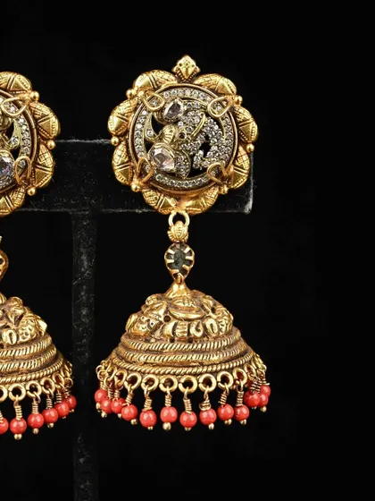 These temple-style jhumkas feature a Ganesha motif on the stud, set with sparkling stones. The bell is finished with bright red beads, adding a touch of auspicious color.