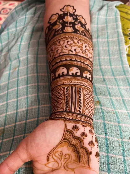 A closer look at the forearm section of a bridal design. It features bands of different traditional patterns, including a row of small elephants, floral vines, and geometric checks.