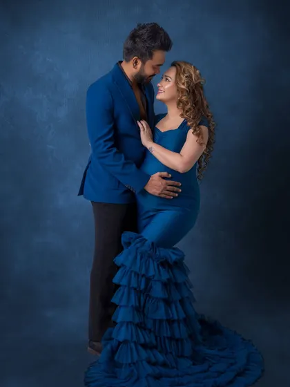 A romantic pose full of connection. The mother-to-be is seated while her partner stands and they gaze into each other's eyes, a classic pose that highlights their bond.