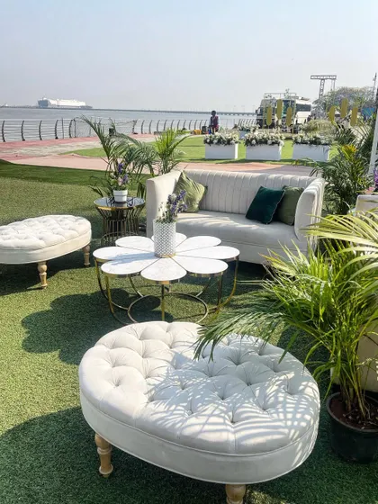 A chic seaside lounge area with modern white furniture and lush green plants. The flower-shaped coffee table adds a playful touch to this clean and sophisticated outdoor setup.