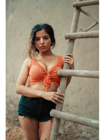 A close-up from the ladder series, where the direct eye contact creates a strong connection. The simple orange top pops against the neutral, textured background.