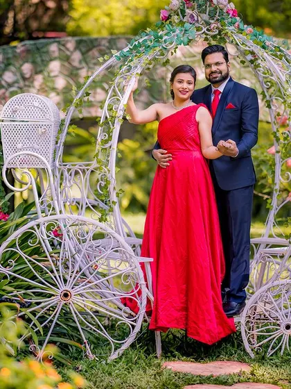A lovely portrait of a couple posing with a Cinderella carriage. The bride's red gown and the beautiful garden create a perfect fairy-tale scene.