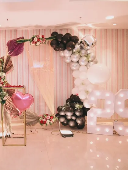 A modern and romantic 29th birthday setup, with a black, white, and silver balloon arch, a personalized photo display, and large marquee numbers.